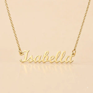 Product photograph of the 18K Yellow Gold Edition personalized name necklace featuring the name 'Isabella' in an elegant cursive script. The polished gold pendant is centered on a delicate 18-inch adjustable cable chain, presented against a soft, light-beige background.